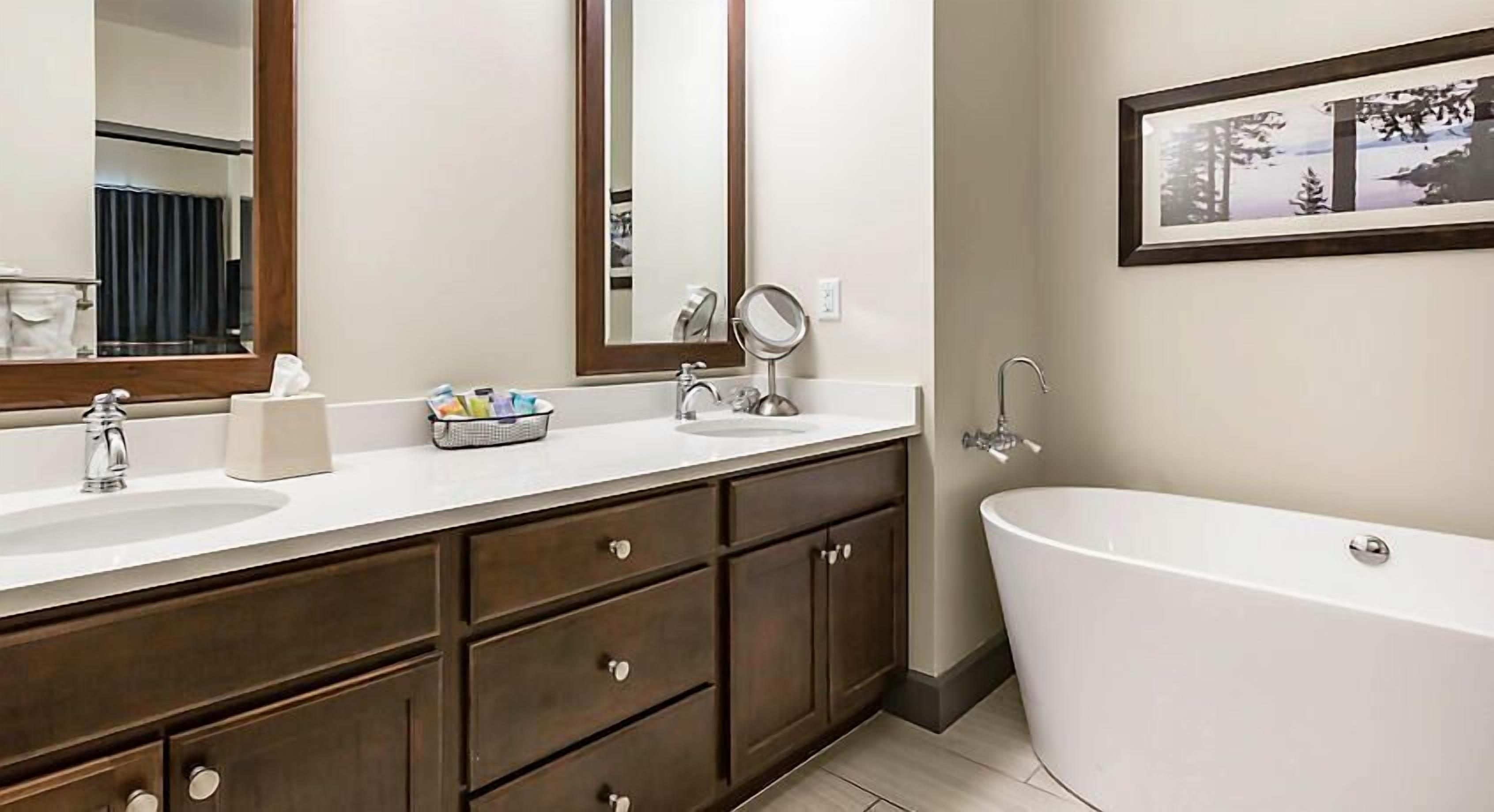 Un baño moderno con un lavamanos espacioso, dos lavabos, una bañera y un espejo.