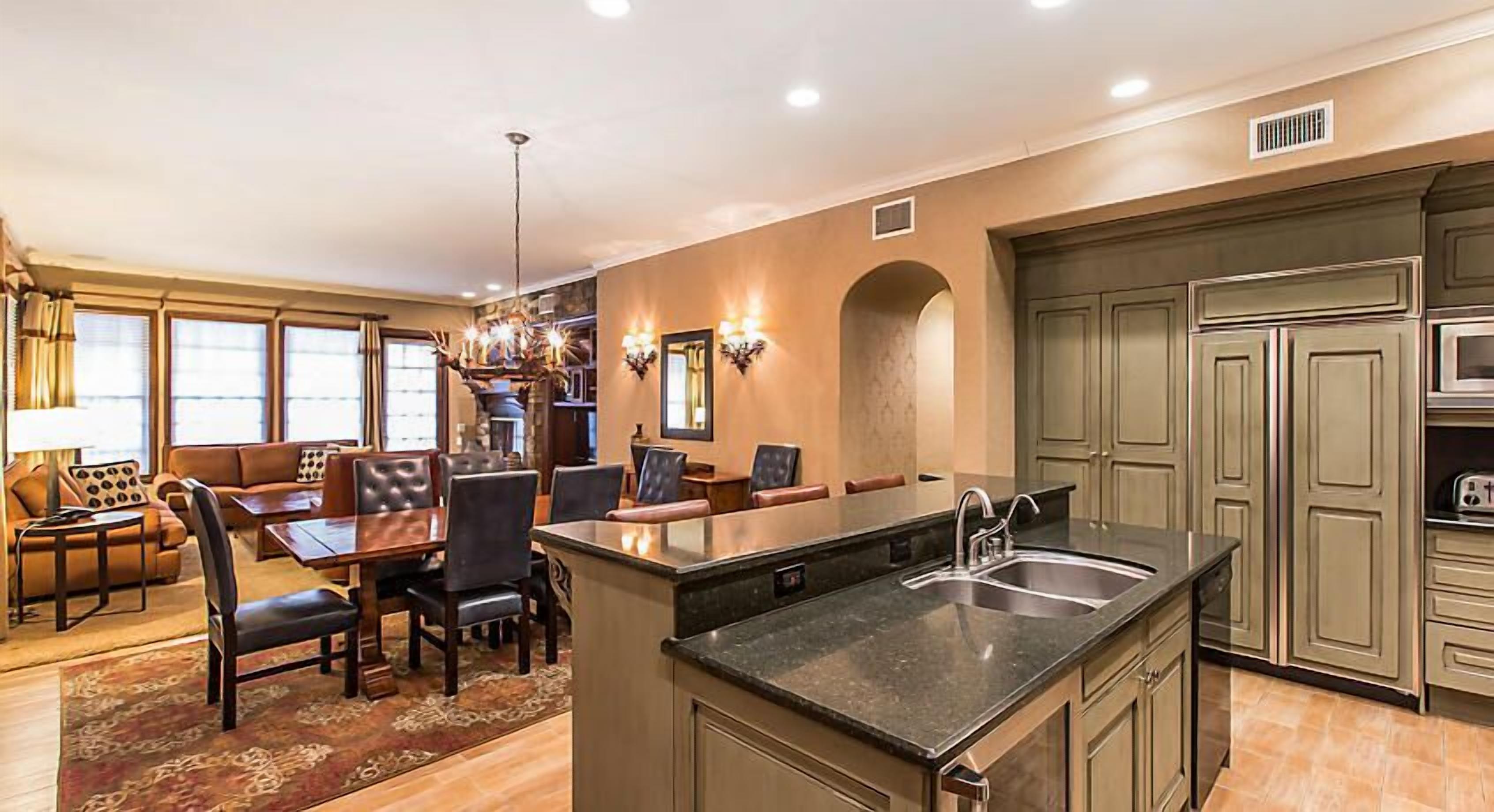 A spacious kitchen with a central island, dining area with a sofa and chairs, and a large window providing natural light.