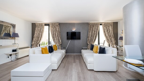 A modern living room with a white sofa set, a flat-screen TV mounted on the wall, and a glass coffee table. - Elegant Two bedroom in the heart of Kensington (London)