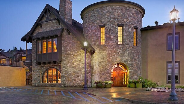 A stone building with a round tower, large windows, and a wooden door.