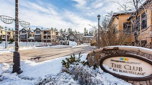 A snow-covered street with a sign for 'The Club at Big Bear Village'.