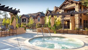 A hot tub surrounded by outdoor seating, a stone building, and a pergola.