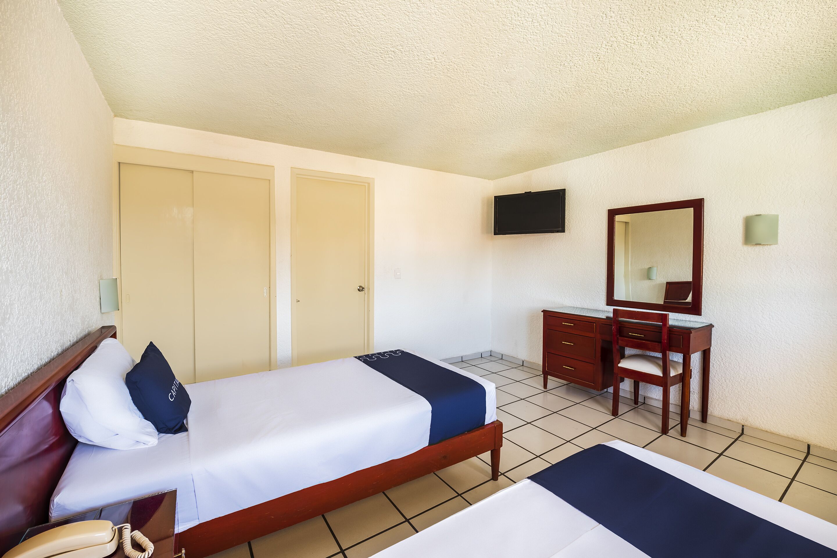 A hotel room with a bed, a desk, a chair, a television, and a wardrobe.