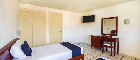 A hotel room with a bed, a desk, a chair, a television, and a wardrobe.