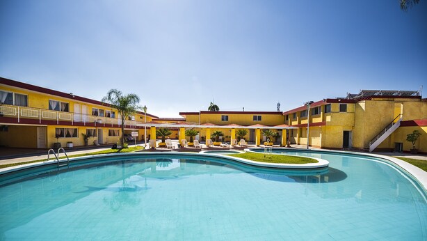 A swimming pool surrounded by yellow buildings with balconies, a clear sky, and a staircase leading to an upper level. - Capital O Colón,  Ciudad Guzmán Jalisco (Zapotlán el Grande)