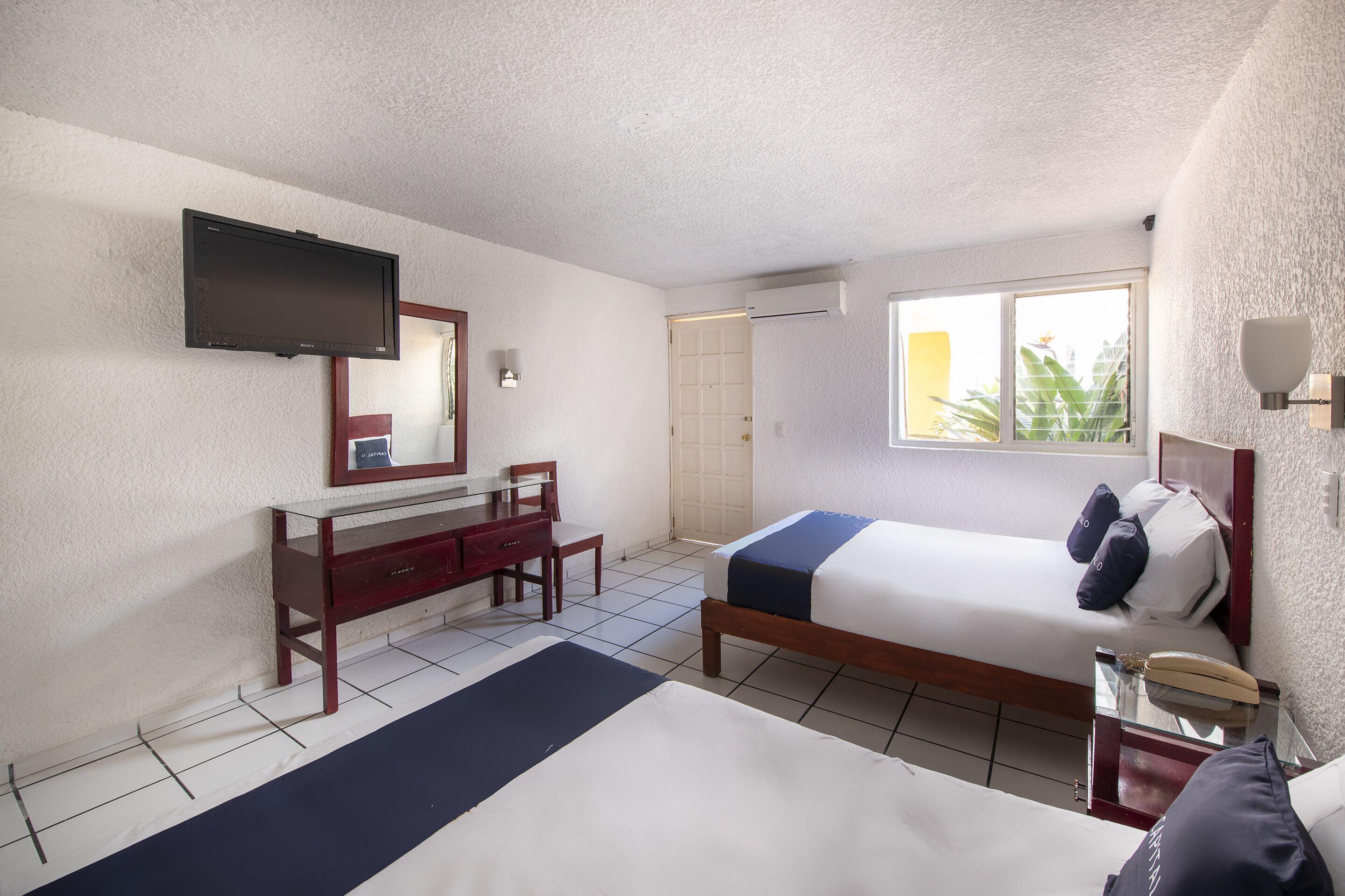 Habitación de hotel con cama, escritorio, silla, televisión y ventana con vistas a zonas verdes.