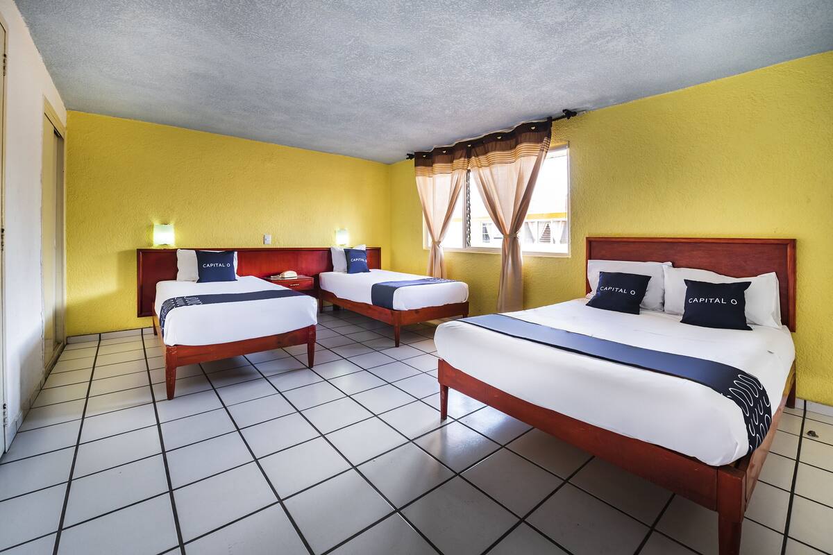 A hotel room with two single beds and one double bed, all with white bedding and dark headboards.