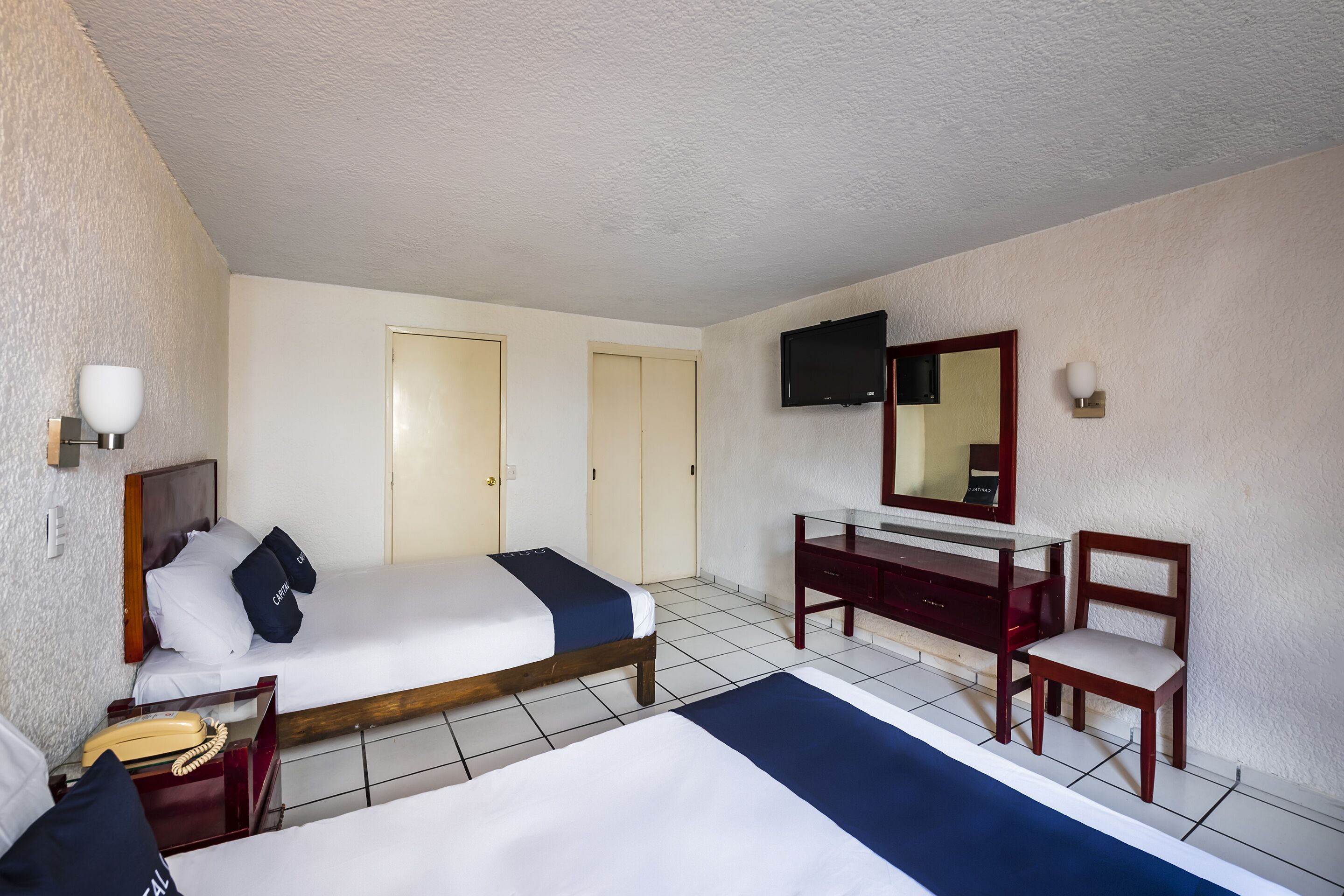 Habitación de hotel con cama, escritorio, silla, televisor y teléfono.