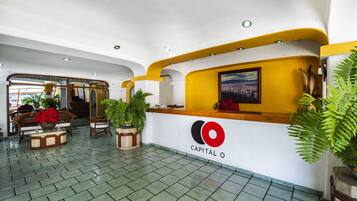 A reception area with a white and yellow color scheme, a reception desk, and potted plants.