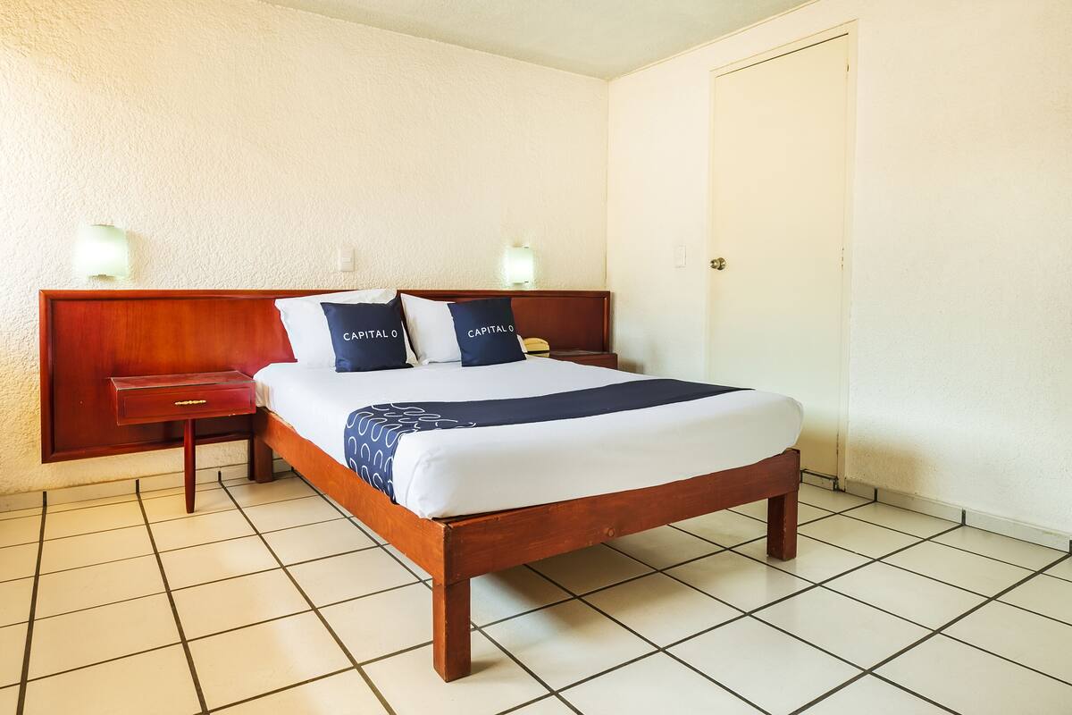 A neatly made bed with a wooden headboard, a bedside table, and two wall-mounted lamps.