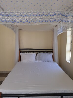 Una cama individual con ropa de cama blanca, cabecera de metal y techo estampado.