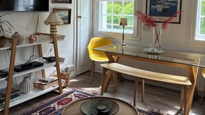 A living room with a TV, a yellow chair, a glass table, a bench, a patterned rug, and a hanging lamp.