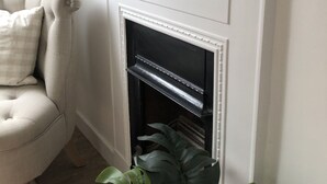 A living room with a white fireplace, a beige armchair, and a large green plant.