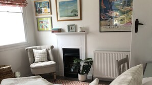 A neatly arranged bedroom with a bed, a chair, a fireplace, and wall art.