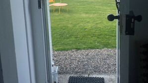 A door leading to a grassy yard with a wooden fence, a yellow chair, and a metal grate at the bottom.
