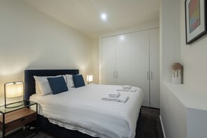A hotel room with a bed, bedside table, lamp, wardrobe, and a wall-mounted artwork. - Spacious CBD Apt in the Heart of Melbourne (Melbourne)