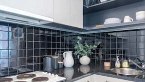 A modern kitchen with black tiles, stainless steel appliances, and a potted plant.