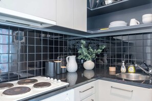 A modern kitchen with black tiles, stainless steel appliances, and a potted plant. - Spacious CBD Apt in the Heart of Melbourne (Melbourne)