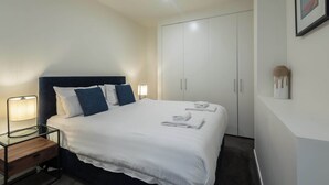 A hotel room with a bed, bedside lamp, wardrobe, and a wall-mounted artwork.