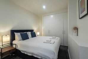 A hotel room with a bed, bedside lamp, wardrobe, and a wall-mounted artwork. - Spacious CBD Apt in the Heart of Melbourne (Melbourne)