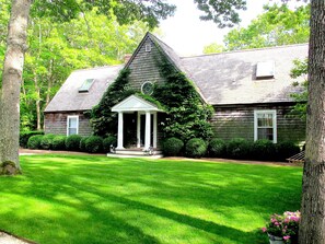 A two-story house with a central porch and a small garden. - Beautiful Family Home Nestled In The Heart Of Sagaponack (Sagaponack)