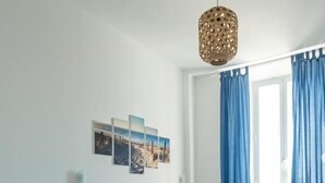 Habitació amb dos llits, una làmpada penjant i una finestra amb cortines.