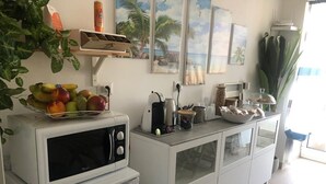 Cuina amb microones, nevera petita i un armari amb portes de vidre. Hi ha fruita sobre la microones, una bullidora i una cafetera a la tauleta.