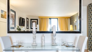 A dining area with a glass table, white chairs, and a large mirror reflecting the room.