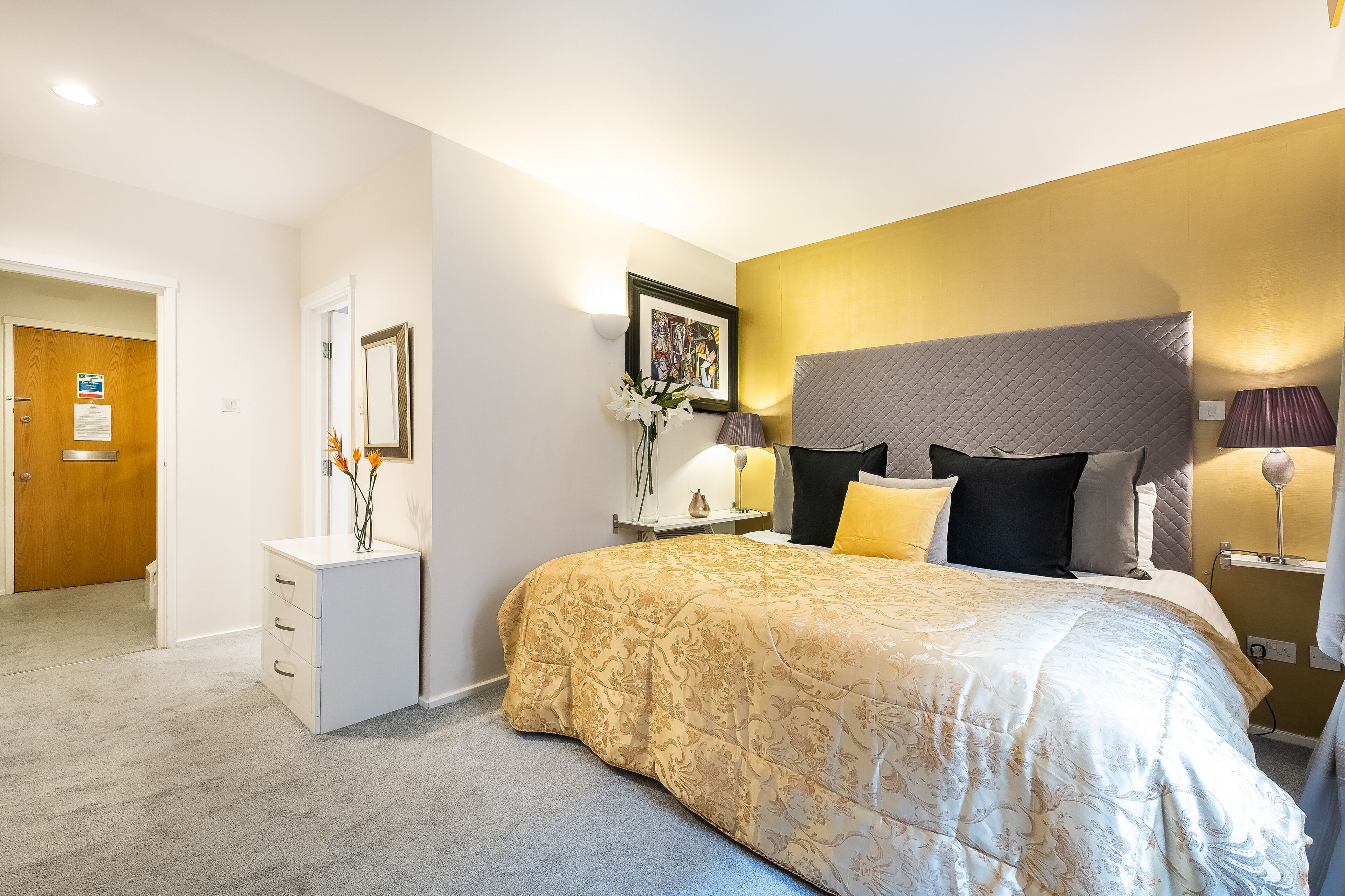 A bedroom with a large bed, bedside lamps, a nightstand, and a framed artwork on the wall.