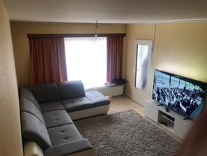 A living room with a sectional sofa, a television, and a radiator.