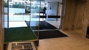 Um espaço de escritório moderno com paredes de vidro, piso de madeira e um tapete preto no centro.