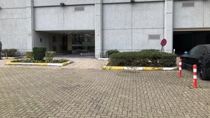 Entrada de um edifício com um caminho de acesso pavimentado, um carro e uma placa de proibido estacionar.