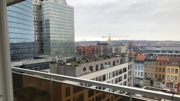 Um edifício alto com fachada de vidro moderna, vista de um horizonte urbano com diversos edifícios e uma grua de construção ao longe.