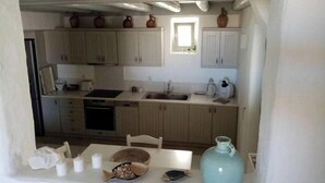 A compact kitchen with light wooden cabinets, a sink, a stove, and a dining table with a fish dish and a blue vase.