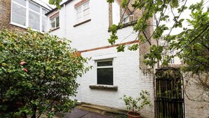 Une ruelle étroite avec un bâtiment en briques blanches, une petite fenêtre et un portail en métal.