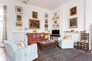 A living room with a red sofa, a light blue armchair, a wooden coffee table, and a patterned rug. There are framed pictures on the walls and a television on a stand. - Artistic 1 Bedroom Apartment (London)