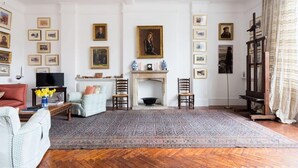 Un salon traditionnel avec une cheminée, des tableaux encadrés aux murs et un tapis à motifs.