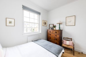 A bedroom with a bed, a dresser, a chair, and a window with a view of buildings. - Cosy and Bright 1 Bed Apartment in Pimlico (London)