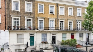 A row of terraced houses with white doors and windows, a green door in the center, and a black car parked in front.