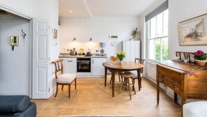 A modern kitchen with white cabinets, a dining table, and chairs. There is a window with a view of greenery outside.