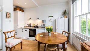 A modern kitchen with white cabinets, a wooden dining table, and a view of greenery outside.