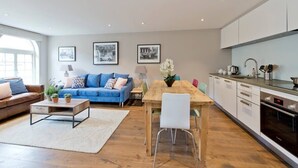 Un salon moderne avec un canapé bleu, une table basse en bois et un coin repas comprenant une table en bois et des chaises blanches.