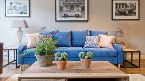 Un salon avec un canapé bleu, deux cactus en pot et trois photographies encadrées accrochées au mur.