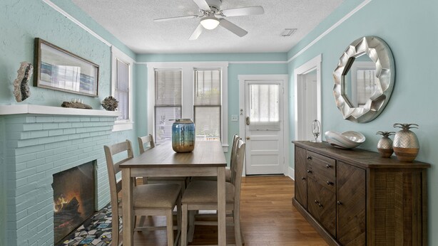 A dining area with a fireplace, wooden table, chairs, and a ceiling fan. - Quaint Bungalow just off Main Street! (Dunedin)