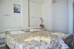 A bedroom with a bed, a nightstand, a potted plant, and a door. - Ionian View Studios (Corfu)