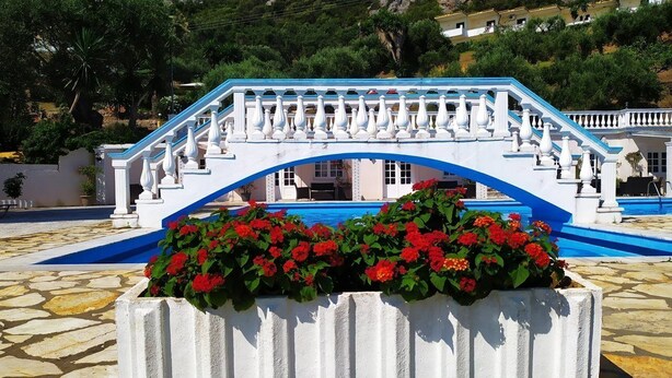 A white bridge with blue accents, a swimming pool, and red flowers in the foreground. - Ionian View Studios (Corfu)