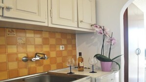 A kitchen with a tiled backsplash, a stainless steel sink, a white countertop, and a potted plant. - Ionian View Studios (Corfu)
