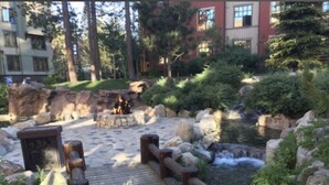 Una terraza de madera que conduce a un estanque con cascada, rodeado de rocas y vegetación.
