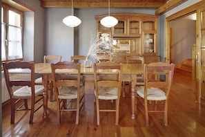 A dining area with a wooden table and chairs, a vase with branches, and wooden cabinets in the background.