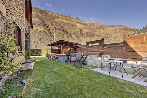 A patio area with a wooden table and chairs, a barbecue grill, and a small wooden structure.
